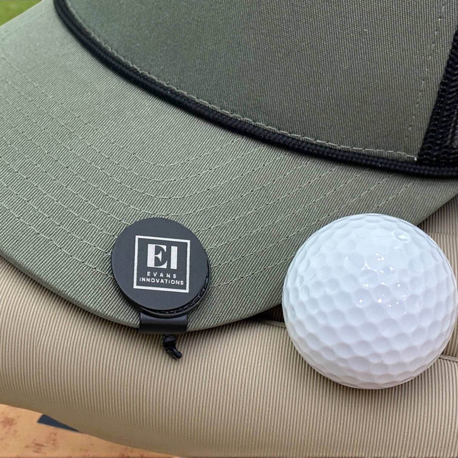 A custom laser engraved magnetic golf marker hat clip sitting on green grass next to a golf ball. Perfect for businesses, corporations, and golf tournaments. Personalized with your logo or design, this stylish and functional golf accessory makes a professional gift for clients, employees, or tournament participants.